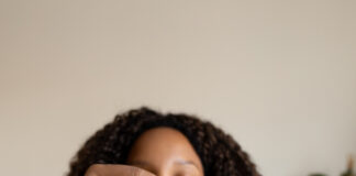 Vertical portrait of young Black woman using pendulum at home. Divination tool for spiritual practice. Spirituality concept.